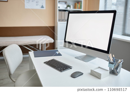 Close up shot of big blank screen computer monitor and office supplies on desk in medical examination room Close up shot of big blank screen computer monitor and office supplies on desk in medical examination room 110698517