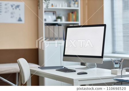 Medium shot of computer monitor with white copy space screen and stationery on table in doctors consulting room Medium shot of computer monitor with white copy space screen and stationery on table in doctors consulting room 110698520