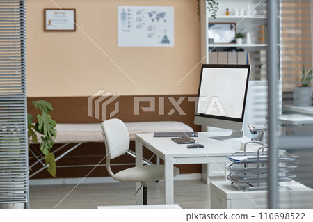 Wide shot of doctors office interior with white screen operating computer on desktop, medical equipment and posters Wide shot of doctors office interior with white screen operating computer on desktop, medical equipment and posters 110698522