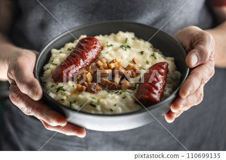 The hands of a senior home cook hold a plate with a national Slovak dish - Bryndzove Halusky. The hands of a senior home cook hold a plate with a national Slovak dish - Bryndzove Halusky. 110699135