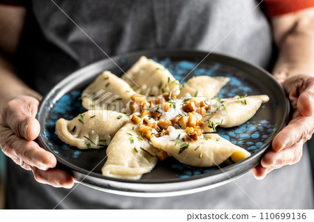 The hands of a senior home cook hold a plate with a national Slovak dish - Bryndzove Pirohy. 110699136