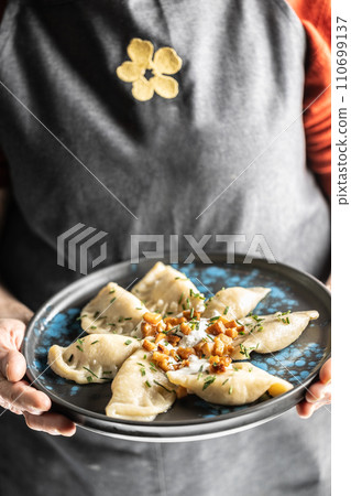 The hands of a senior home cook hold a plate with a national Slovak dish - Bryndzove Pirohy. The hands of a senior home cook hold a plate with a national Slovak dish - Bryndzove Pirohy. 110699137