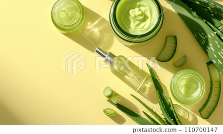 Aloe beauty essentials flat lay, jars and bottles of aloe products with aloe sprigs. Yellow backdrop 110700147