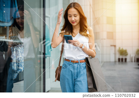 Young woman scrolling through her smartphone while standing against a wall in the city. Her phone is her window to the virtual world of social media and entertainment. Young woman scrolling through her smartphone while standing against a wall in the city. Her phone is her window to the virtual world of social media and entertainment. 110702032