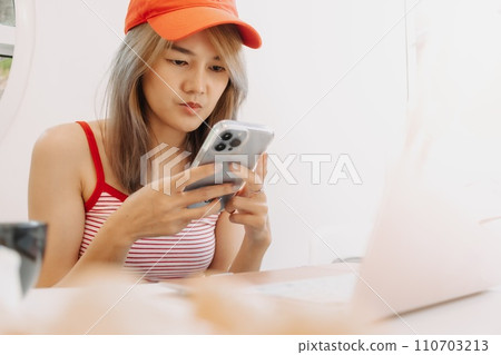Cute freelance girl is using smartphone while working on laptop. 110703213