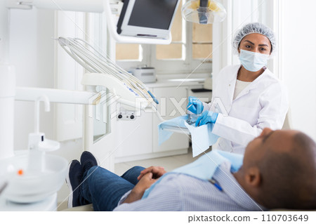 Dentist in uniform is examinating man on chair 110703649