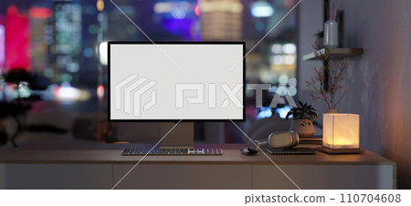 A computer desk in a modern, dark apartment living room at night with a night-light city view. 110704608