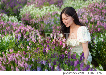 beautiful woman in dress enjoying Angelonia flower blooming in field 110704763