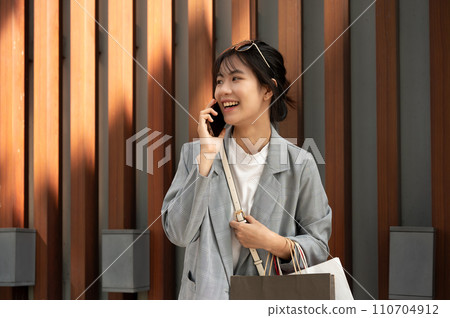 Beautiful Asian woman is talking on the phone while she is having a fun shopping day in the city. 110704912