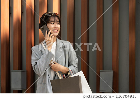 Beautiful Asian woman is talking on the phone while she is having a fun shopping day in the city. Beautiful Asian woman is talking on the phone while she is having a fun shopping day in the city. 110704913
