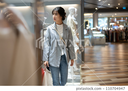A beautiful young Asian woman in trendy clothes is walking in a shopping mall with her shopping bags A beautiful young Asian woman in trendy clothes is walking in a shopping mall with her shopping bags 110704947