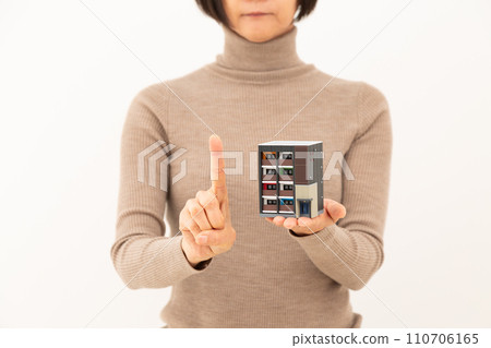 一位中年婦女拿著公寓大樓模型，舉起食指 110706165