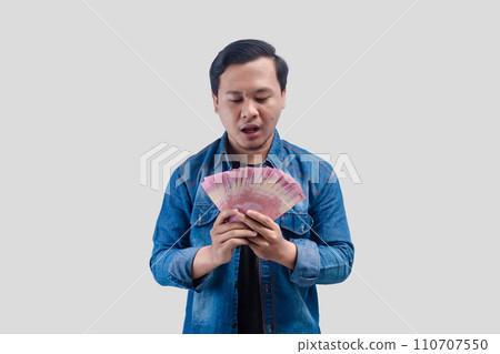 Young Asian man showing stunned face expression while holding paper money 110707550