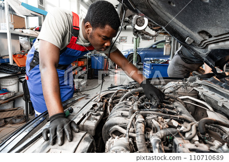 Young African auto mechanic checking car engine under the hood in auto service 110710689