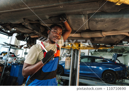 Young African mechanic in uniform working under the car in car service center 110710690
