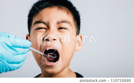 In a pediatric dentist's clinic a doctor examines a child's mouth post removal of loose milk tooth. Dental tools help in detailed examination process. Doctor uses mouth mirror to checking teeth cavity 110710880