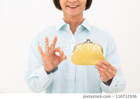 A middle-aged woman holding a purse and making a circle sign 110712936