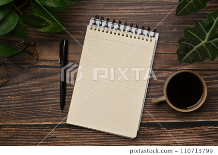 Top view notepad, cup of coffee, pen glasses and houseplant on wooden table 110713799