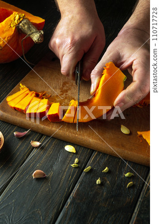 The cook hands use a knife to cut pumpkin into small pieces on a cutting board for baking a pie. American national dish cooking concept The cook hands use a knife to cut pumpkin into small pieces on a cutting board for baking a pie. American national dish cooking concept 110717728
