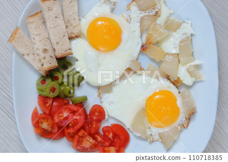 Fried eggs with lard, tomato and green olives in a plate. Homemade breakfast. Domestic food. Top view. Fried eggs with lard, tomato and green olives in a plate. Homemade breakfast. Domestic food. Top view. 110718385