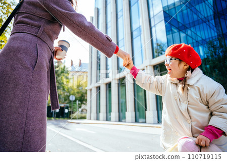 Cute little girl in red wear beret and coat in eyeglasses, whirling frolicking and playing with her unrecognizable mother at autumn sunny day city street outdoor. Cute little girl in red wear beret and coat in eyeglasses, whirling frolicking and playing with her unrecognizable mother at autumn sunny day city street outdoor. 110719115