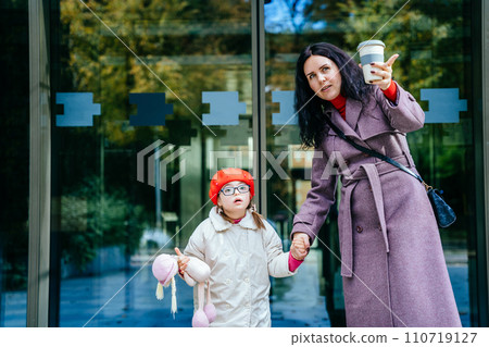 Cute lovely positive brunette mother talking with her happy disabilities daughter outdoor. Woman and child enjoy walk autumn sunny day outside the business center. 110719127