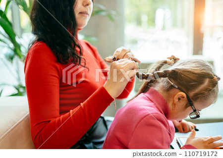 Happy family moments concept. Candid side view portrait of happy mother and daughter relaxing weave braids in cafe together and using smartphone. 110719172