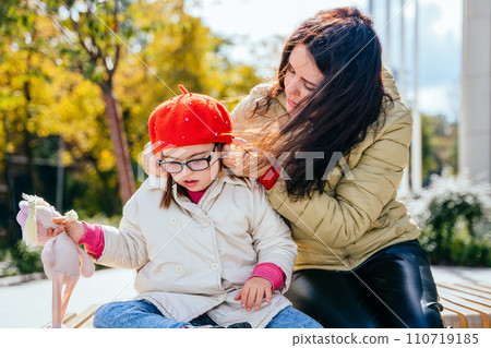Portrait of young mother who sitting on bench outdoor with cute beautiful disabled daughter and communication to each other. 110719185