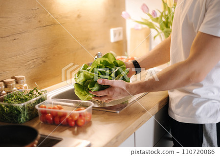 Man washing organic green salad Romano in kitchen. Lettuce leaves with water drops 110720086