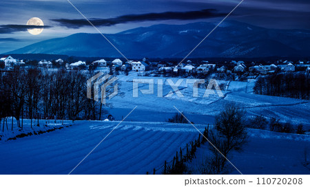 mountainous countryside scenery in winter at night. landscape with snow covered rural fields in full moon light 110720208