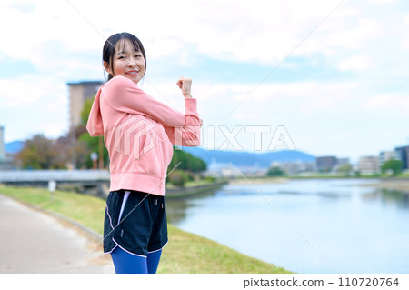 Young woman stretching before jogging along the river, diet running wear Young woman stretching before jogging along the river, diet running wear 110720764