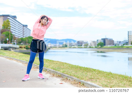 Young woman stretching before jogging along the river, diet running wear 110720767