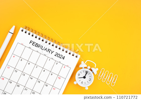 February 2024, Monthly desk calendar for 2024 year and alarm clock with paper clips on yellow color background. February 2024, Monthly desk calendar for 2024 year and alarm clock with paper clips on yellow color background. 110721772