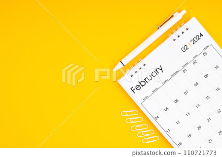 February 2024, Monthly desk calendar for 2024 year and pen with paper clips on yellow color background. February 2024, Monthly desk calendar for 2024 year and pen with paper clips on yellow color background. 110721773