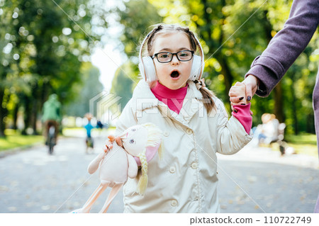 Cute little girl with special needs singing, listening music with headphones holding toy. Cute little girl with special needs singing, listening music with headphones holding toy. 110722749
