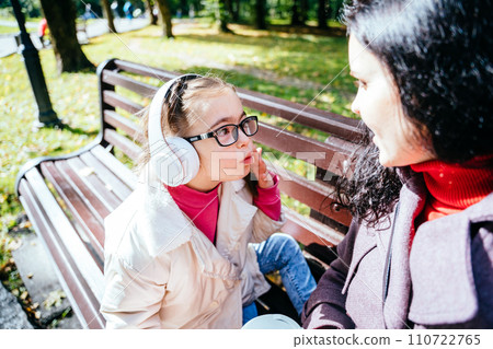 Charming caucasian mother communicating with her little girl with special needs in googles. Parent and child in park. Understanding the needs of the child. 110722765