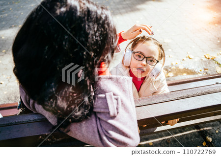 Unrecognizable brunette mother caressing her daughter in headphones outdoor. Family happy moments concept. 110722769