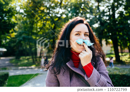 Portrait of middle age mother making blue cotton candy mustache gesturing on camera in amusement park at autumn. 110722799