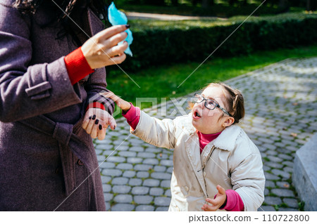 Sad crying little girl with two braids in eyeglasses looking up at unrecognizable mother at autumn park outdoor. Sad crying little girl with two braids in eyeglasses looking up at unrecognizable mother at autumn park outdoor. 110722800