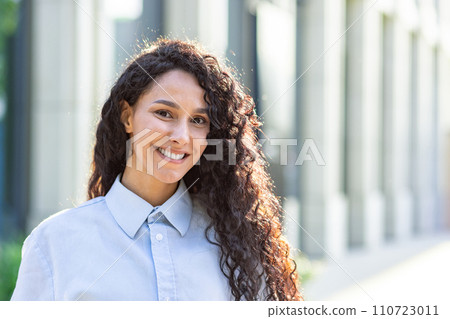 Portrait of a confident and successful young Latin American woman with curly hair outside a city office building. 110723011