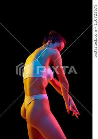 Back view of sensual slim woman posing in white panties and top. Female model with perfect figure against black background in neon light 110723675