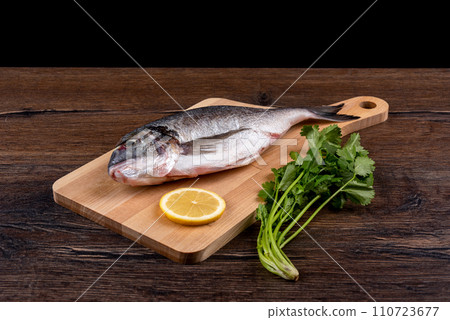 Dorado fish and a slice of lemon on a cutting board, a bunch of cilantro on the table. 110723677