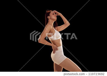 Slim, beautiful female model posing against black studio background. Woman wearing in sporty clothes, shorts and top. 110723692