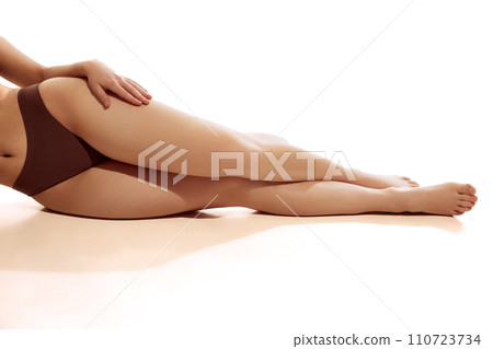 Cropped photo of slim and smooth female legs. Model posing in brown lingerie against white studio background. 110723734