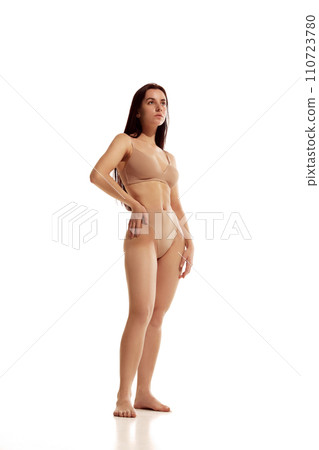 Full length portrait of young attractive woman posing in beige lingerie against white studio background. Female model with perfect body shapes. 110723780