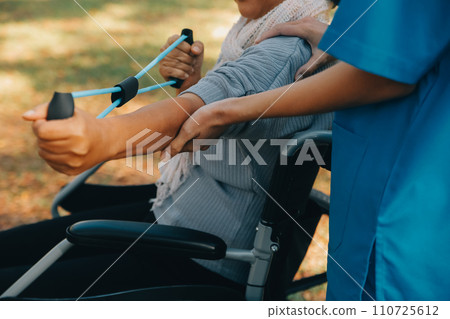 Young nurse or physiotherapist in scrubs helping a happy retired old woman do fitness exercises with light weight dumbbells at home. Concept of physiotherapy for seniors Young nurse or physiotherapist in scrubs helping a happy retired old woman do fitness exercises with light weight dumbbells at home. Concept of physiotherapy for seniors 110725612