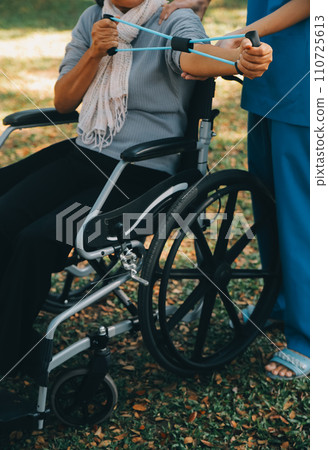 Young nurse or physiotherapist in scrubs helping a happy retired old woman do fitness exercises with light weight dumbbells at home. Concept of physiotherapy for seniors Young nurse or physiotherapist in scrubs helping a happy retired old woman do fitness exercises with light weight dumbbells at home. Concept of physiotherapy for seniors 110725613