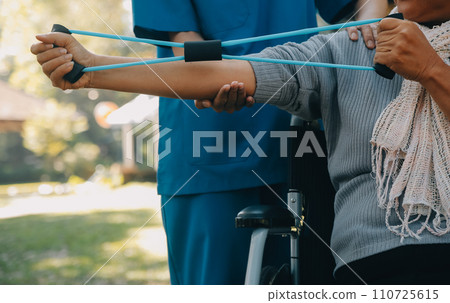 Young nurse or physiotherapist in scrubs helping a happy retired old woman do fitness exercises with light weight dumbbells at home. Concept of physiotherapy for seniors Young nurse or physiotherapist in scrubs helping a happy retired old woman do fitness exercises with light weight dumbbells at home. Concept of physiotherapy for seniors 110725615