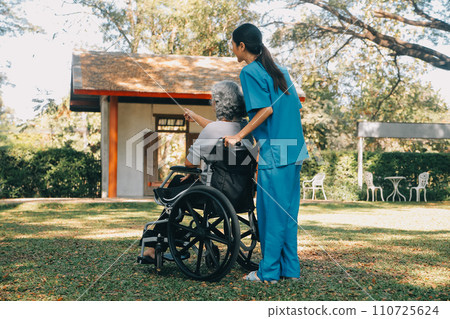 Young asian care helper with asia elderly woman on wheelchair relax together park outdoors to help and encourage and rest your mind with green nature. Help support yourself to learn to walk. walker Young asian care helper with asia elderly woman on wheelchair relax together park outdoors to help and encourage and rest your mind with green nature. Help support yourself to learn to walk. walker 110725624