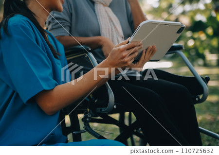 Elderly asian senior woman on wheelchair with Asian careful caregiver and encourage patient, walking in garden. with care from a caregiver and senior health insurance in sun light 110725632